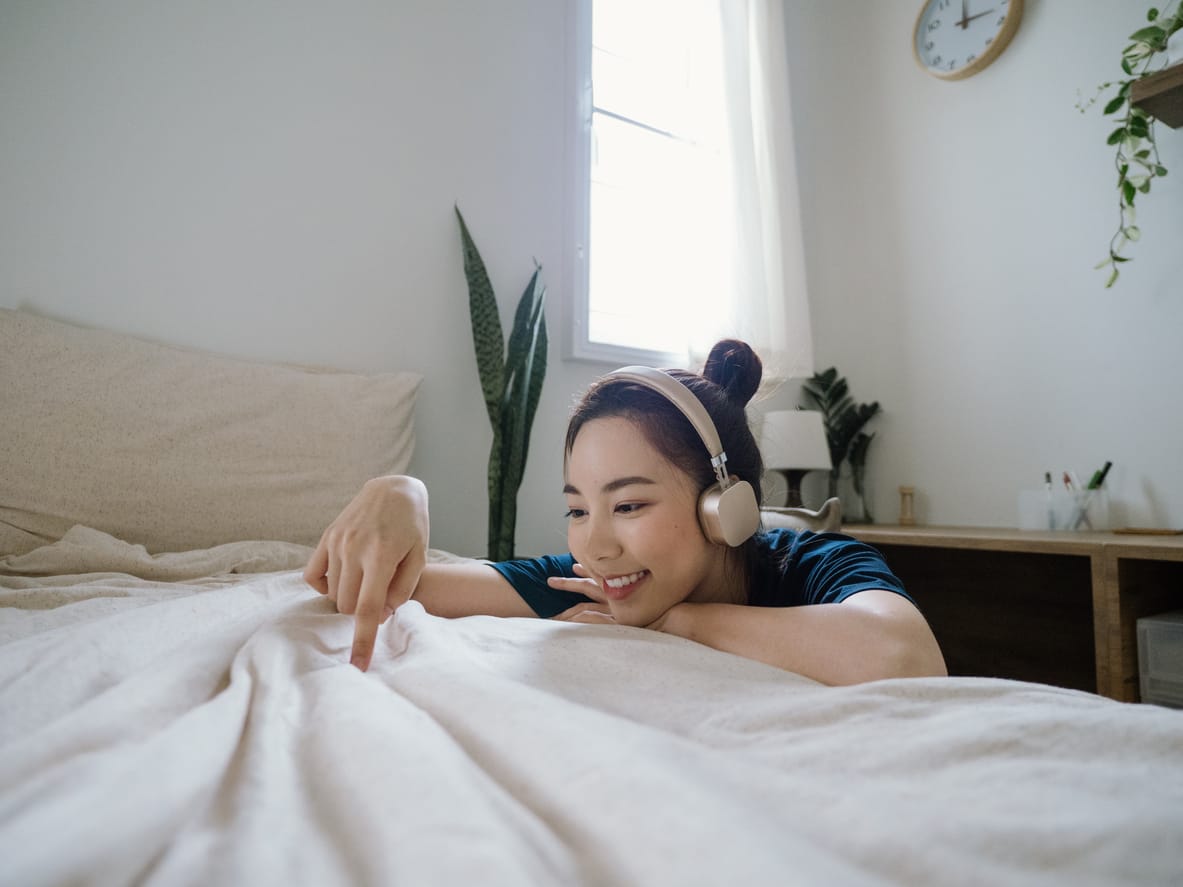 Bild på kvinna som sitter på golvet bredvid en säng med hörlurar på.